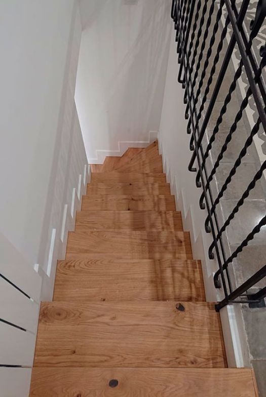 Escalera de madera restaurada con barandilla metálica negra y paredes blancas.