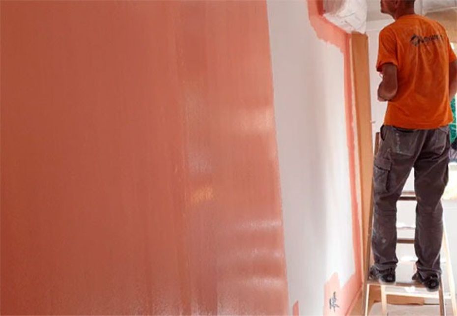 Pintor profesional aplicando pintura color terracota sobre pared blanca en interior de vivienda en Madrid