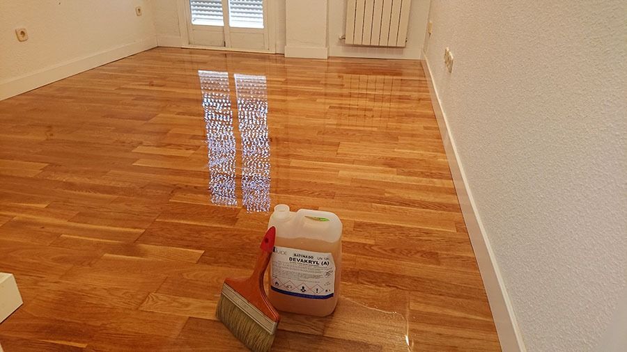 Detalle de suelo de parquet con acabado brillante reflejando la luz de la ventana.