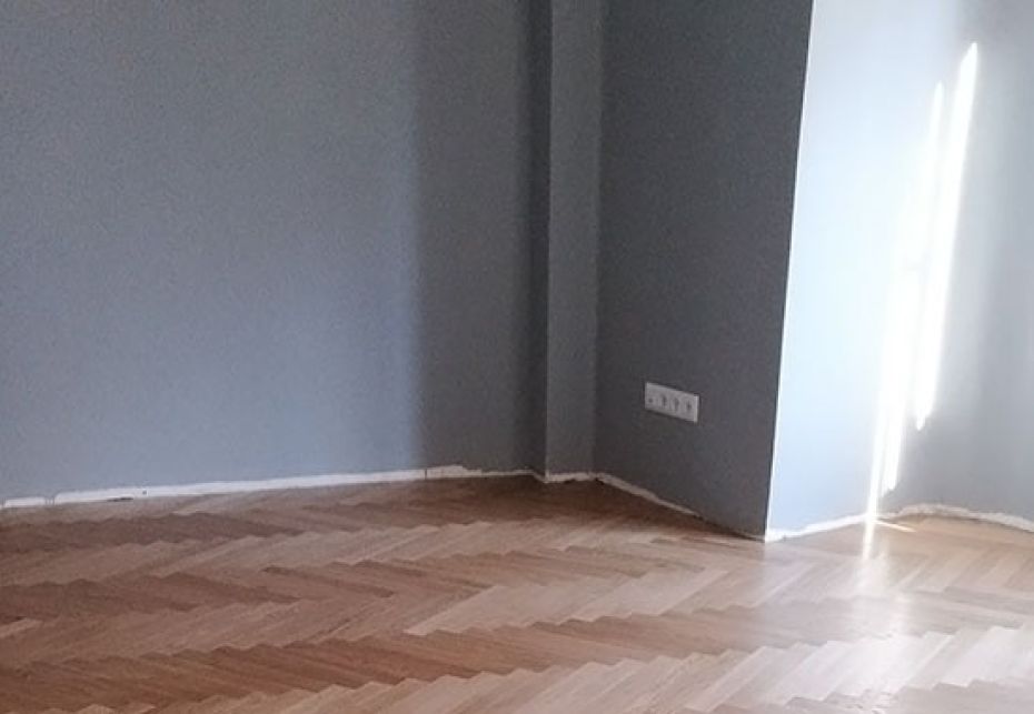 Habitación vacía con paredes pintadas en gris claro y suelo de parquet restaurado en patrón de espiga